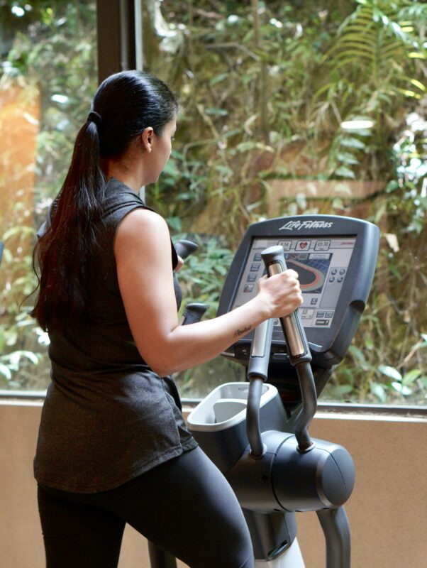 Woman seen from behind using an elliptical machine facing a window