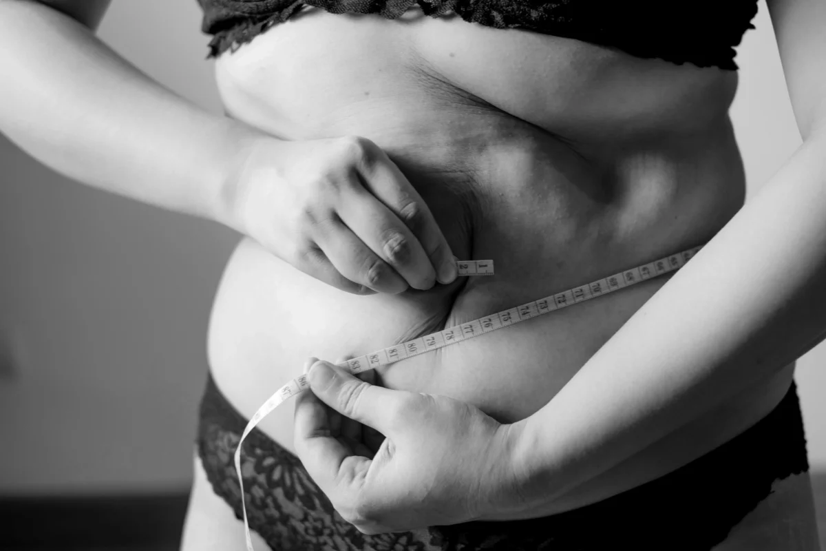 Person measuring belly with tape measure as part of a weight loss journey, focusing on body transformation and fitness progress.